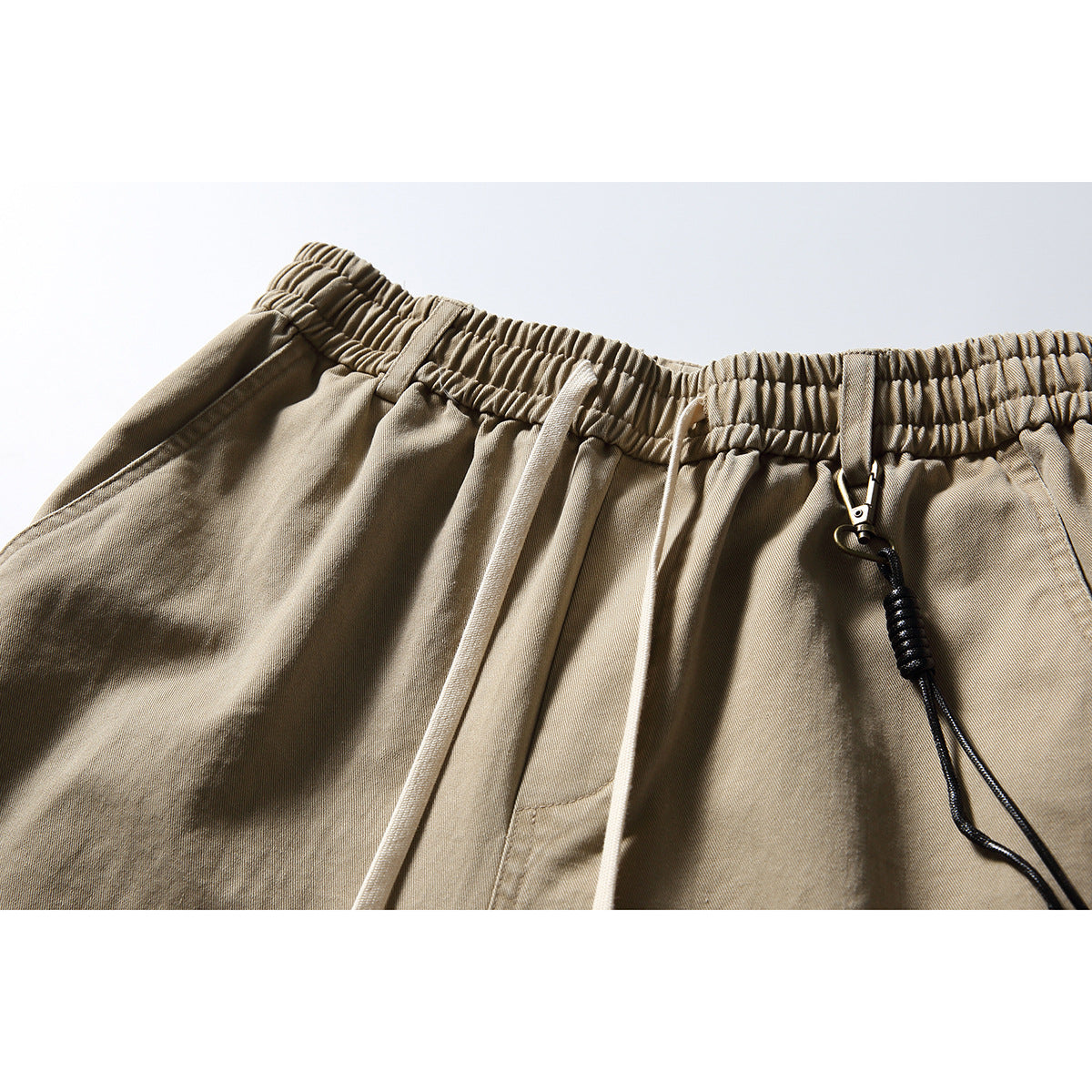Close-up of tan trousers with an elastic waistband, light drawstrings, and a black cord clip.