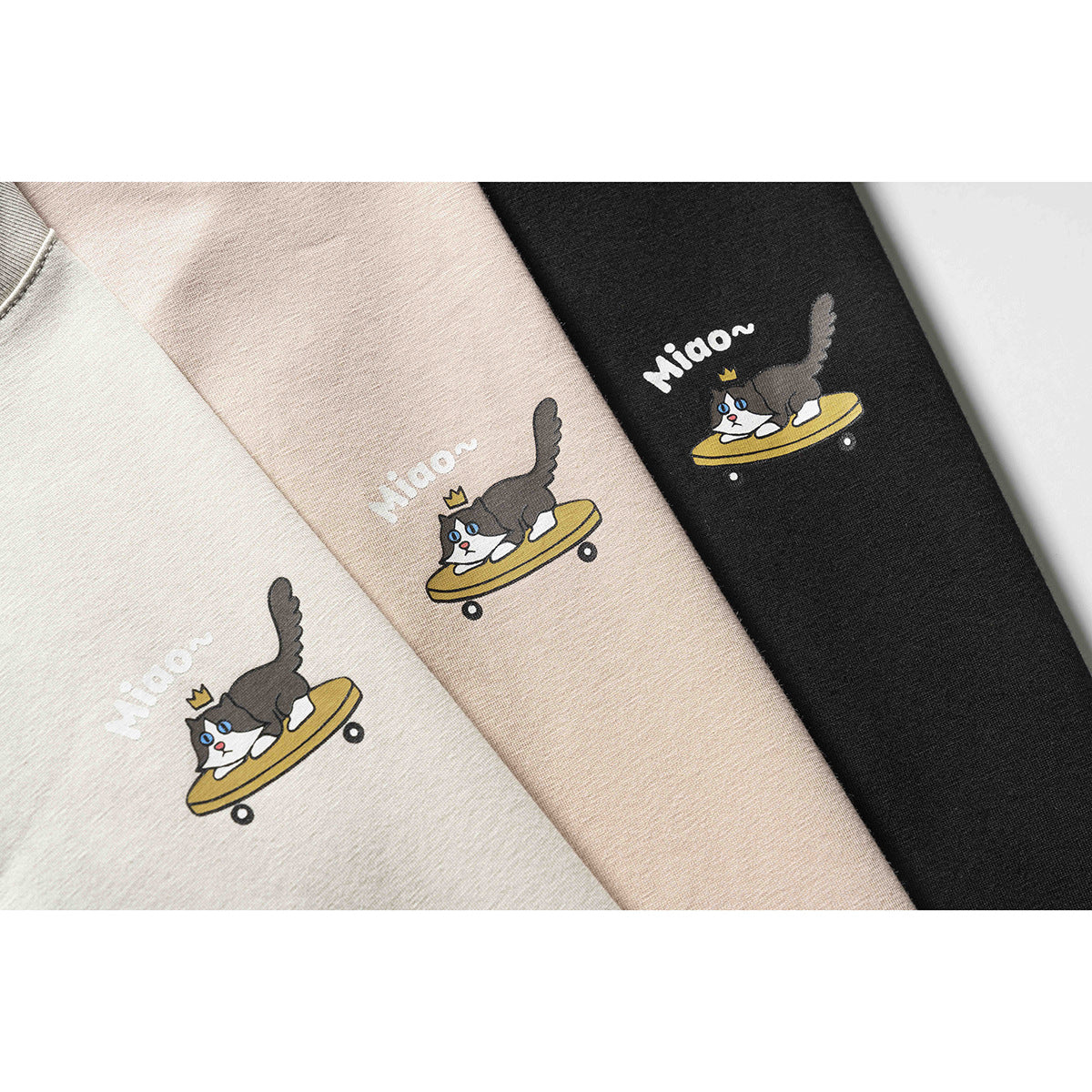 Three folded T-shirts in light beige, blush, and black, each printed with a crowned cat riding a skateboard and “Miaow~.”