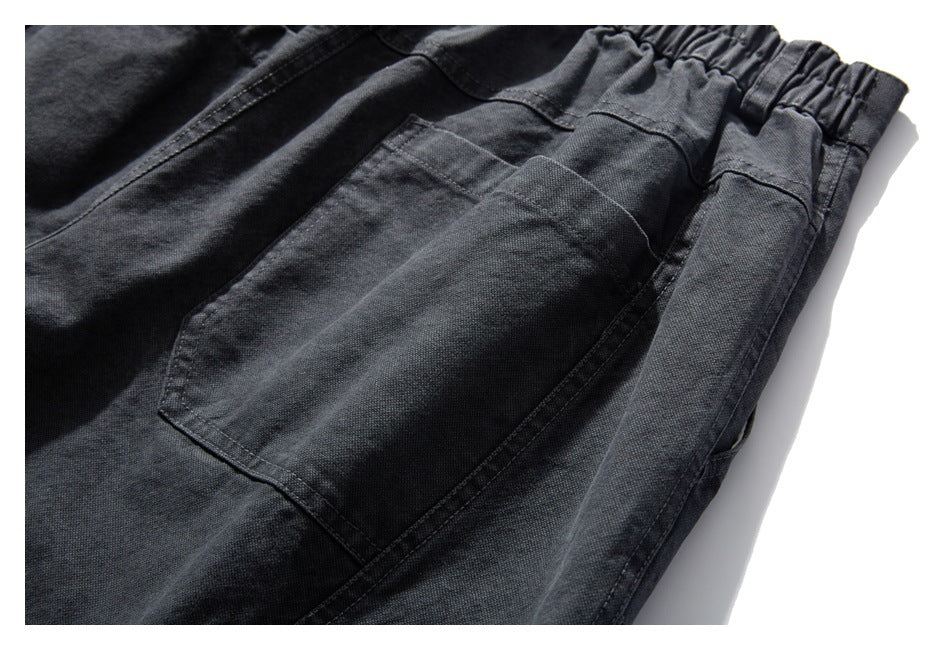 Close-up of charcoal-black pants showing a gathered elastic waistband, stitched seams, and a large rectangular pocket.