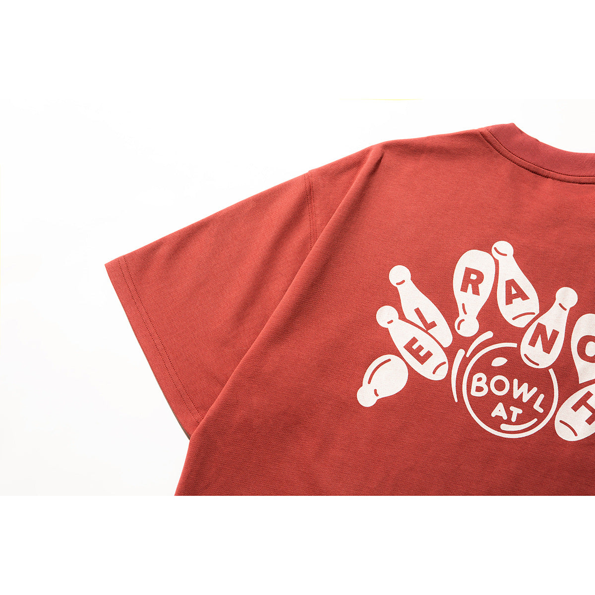 Close-up of a muted red T-shirt’s back with a large white bowling-pin graphic and lettering.
