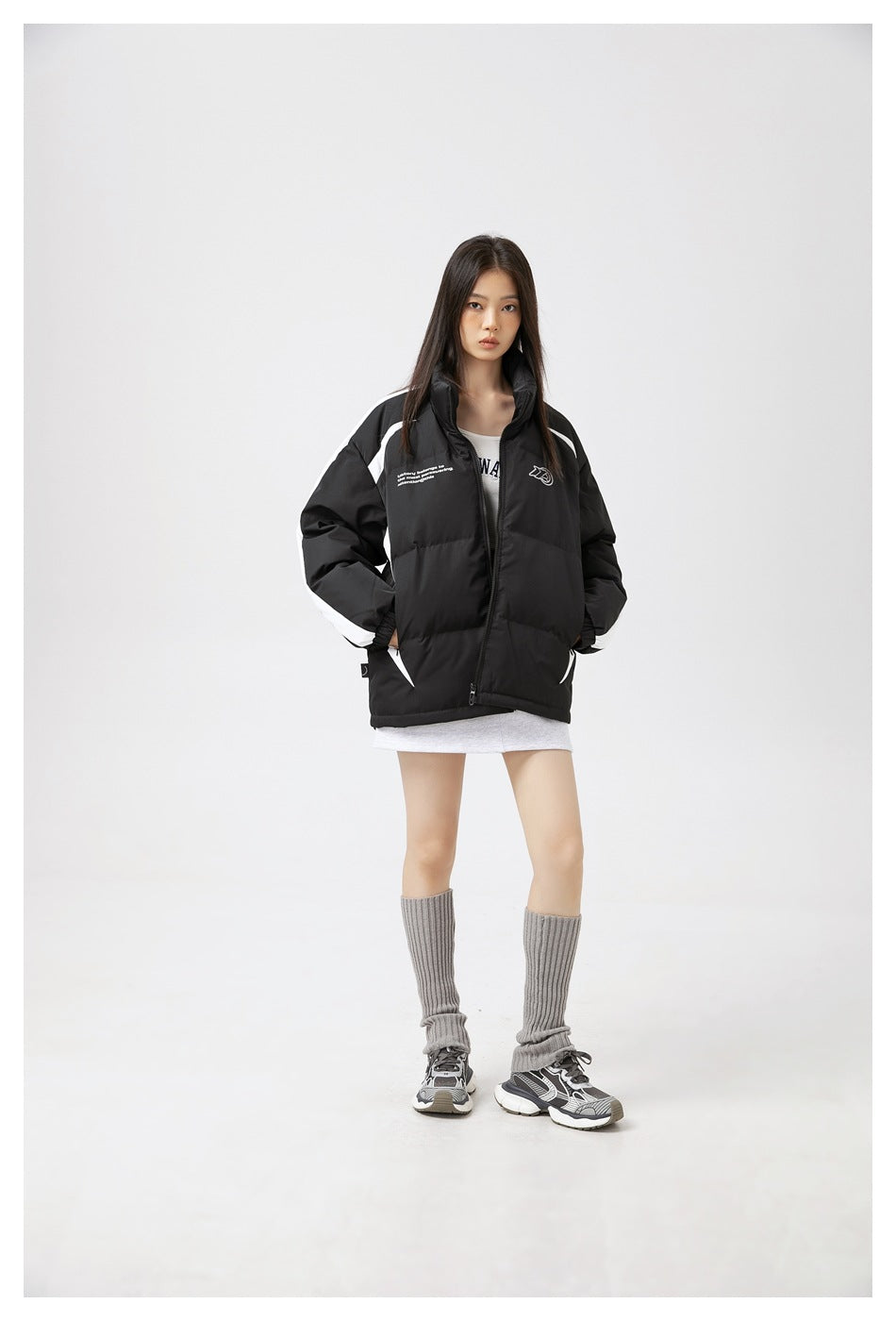 Model wearing a black puffer jacket with white contrast panels, hands in pockets, with gray leg warmers and sneakers