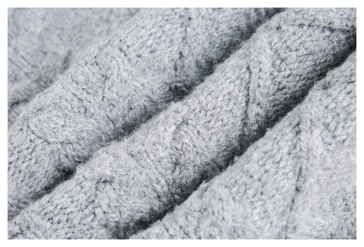 Close-up of thick light gray knit fabric with raised cable stitches and deep folds.