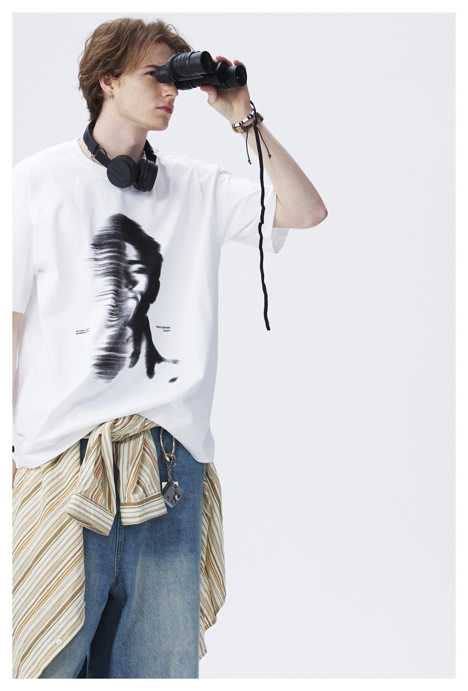 Model wearing a white distorted-portrait graphic T-shirt, shown from the waist up while holding binoculars.
