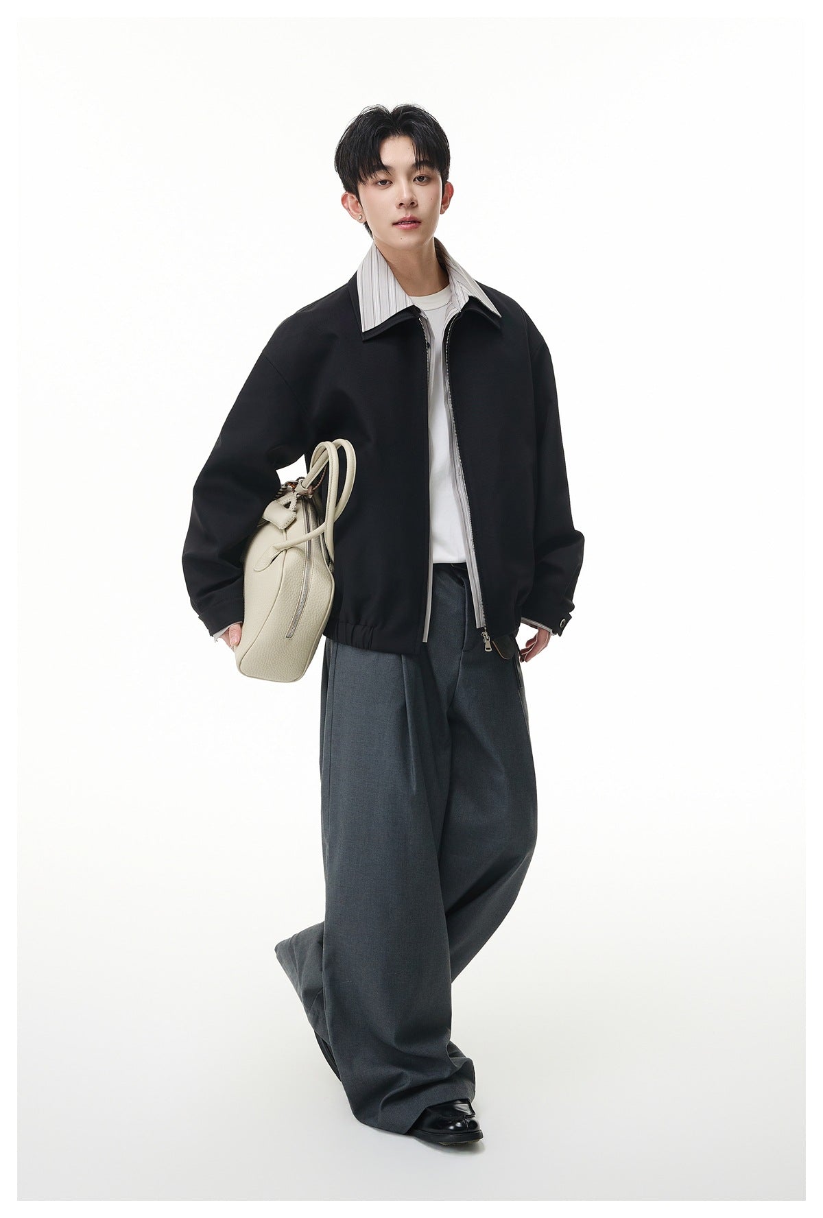 Model wearing a black zip-front jacket with a striped light collar, white shirt and wide charcoal trousers.