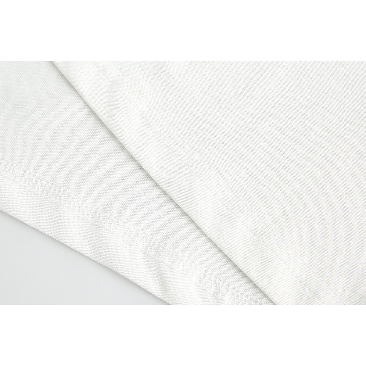 Close-up of white T-shirt fabric and diagonal stitched hem seam.