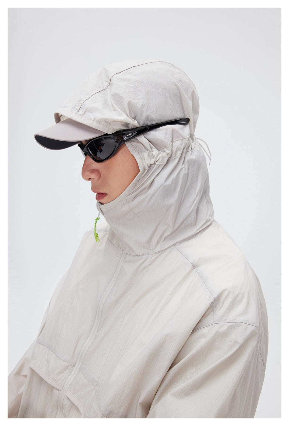 Close view of a model wearing a pale beige jacket zipped to the chin, with a hood and cap.