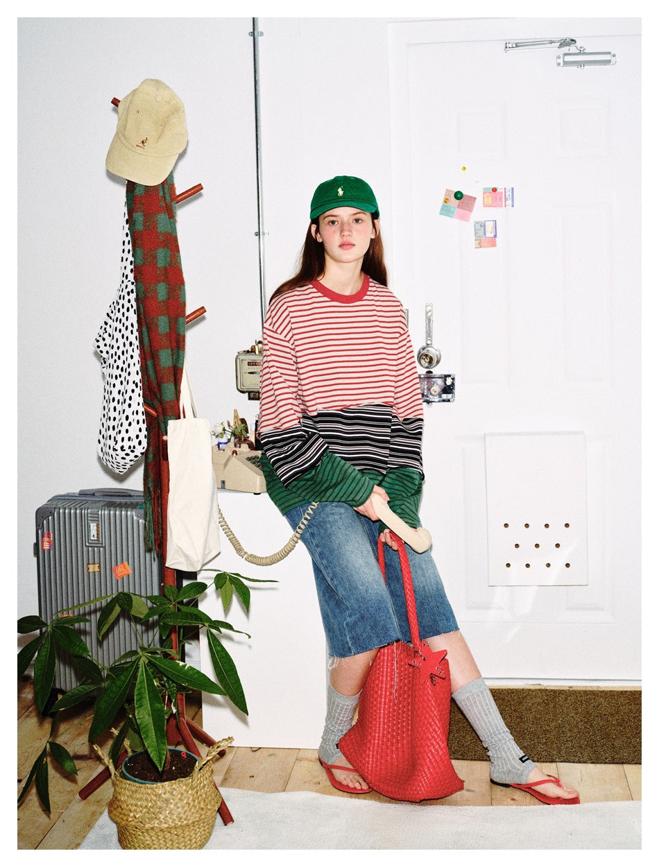 Model seated in an oversized red, cream, black, and green striped color-block shirt.