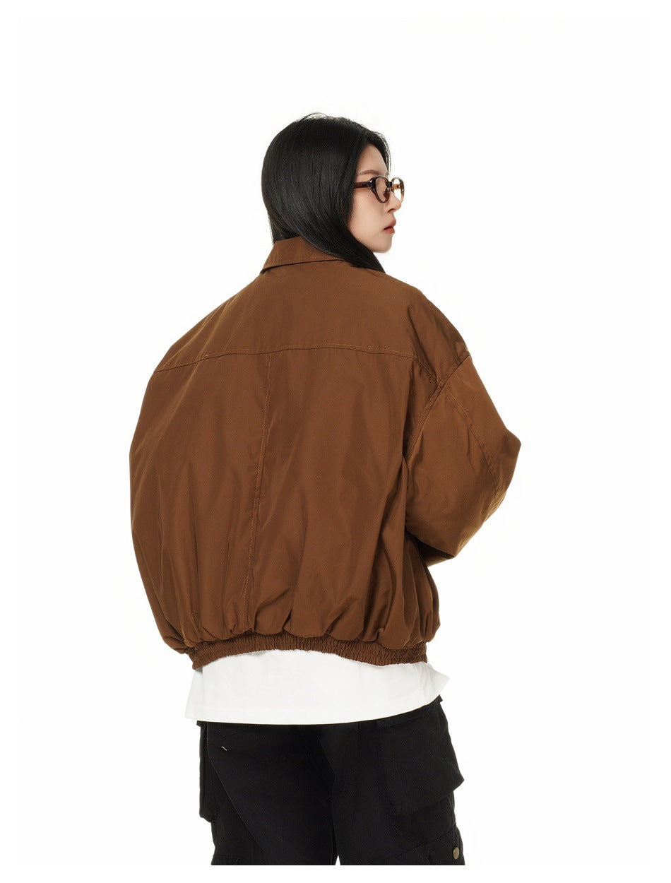 Rear view of a model wearing an oversized brown jacket with a pointed collar and gathered elastic hem.