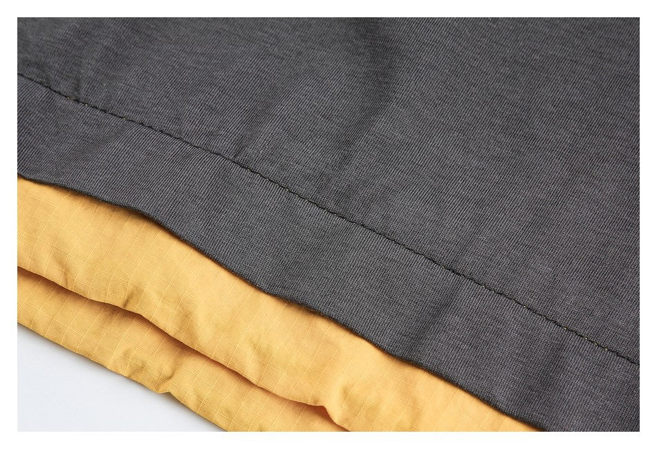 Close-up of a charcoal garment hem layered over mustard-yellow fabric, showing the stitched edge.