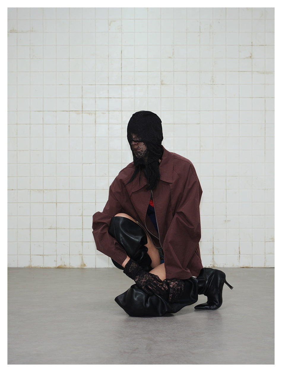 Model crouching in a loose wine-red jacket with lace head covering, lace gloves and black boots on a tiled backdrop