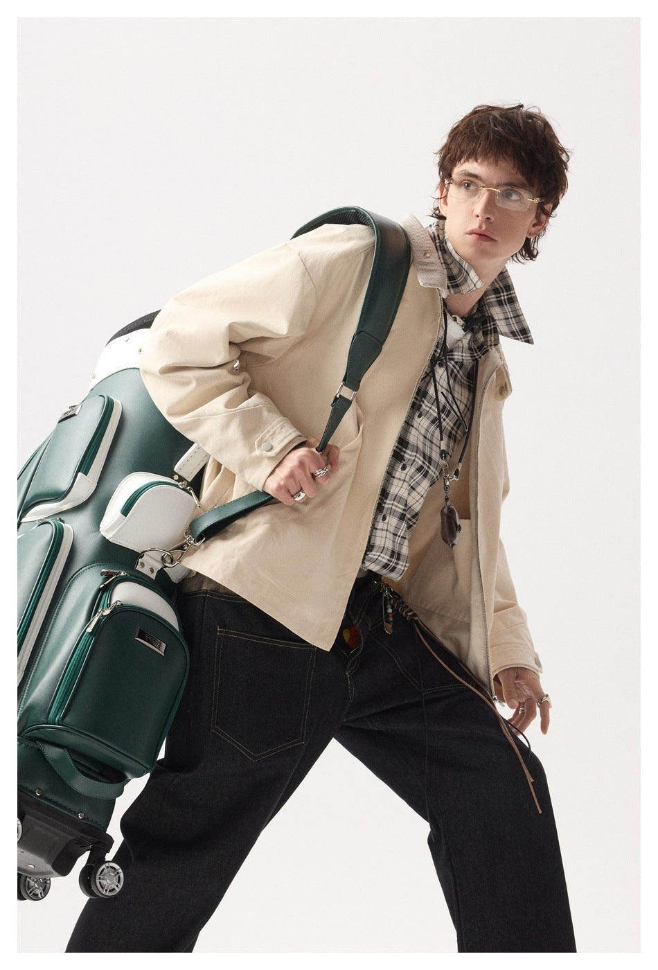Model in a beige zip jacket over a plaid shirt, leaning forward with a green golf bag on one shoulder
