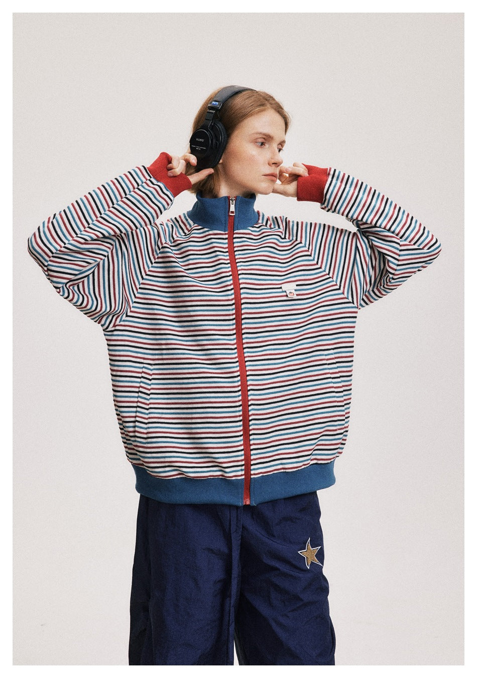 Model wearing a white zip jacket with red, blue and black stripes, blue collar and hem, and red cuffs.