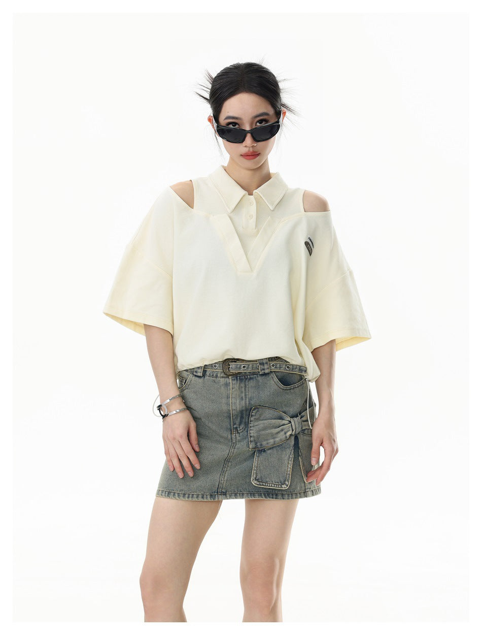 Model wearing an ivory cutout-shoulder polo and a gray denim mini skirt, shown standing.