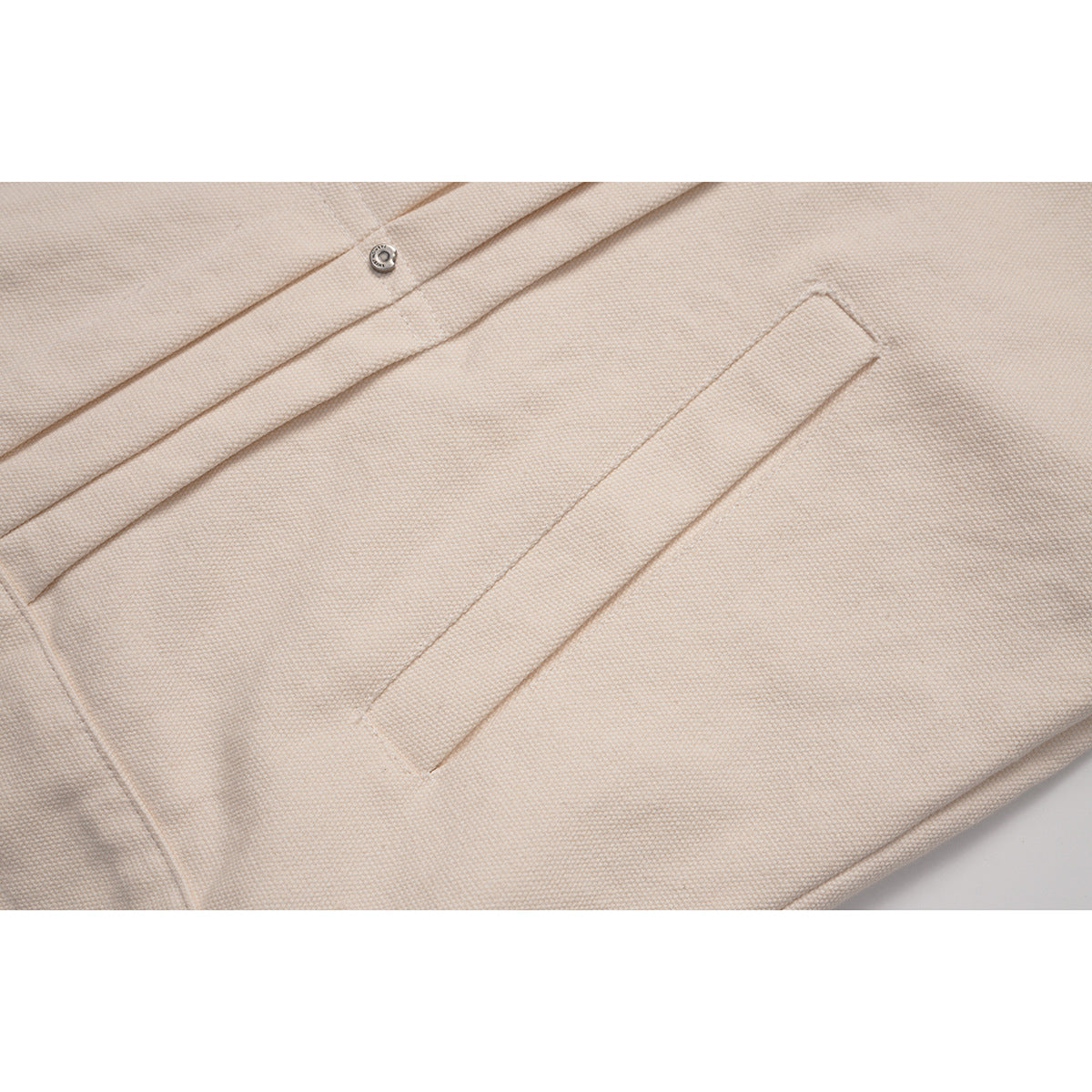 Close-up of a cream jacket's textured fabric, front seam, and angled welt pocket.