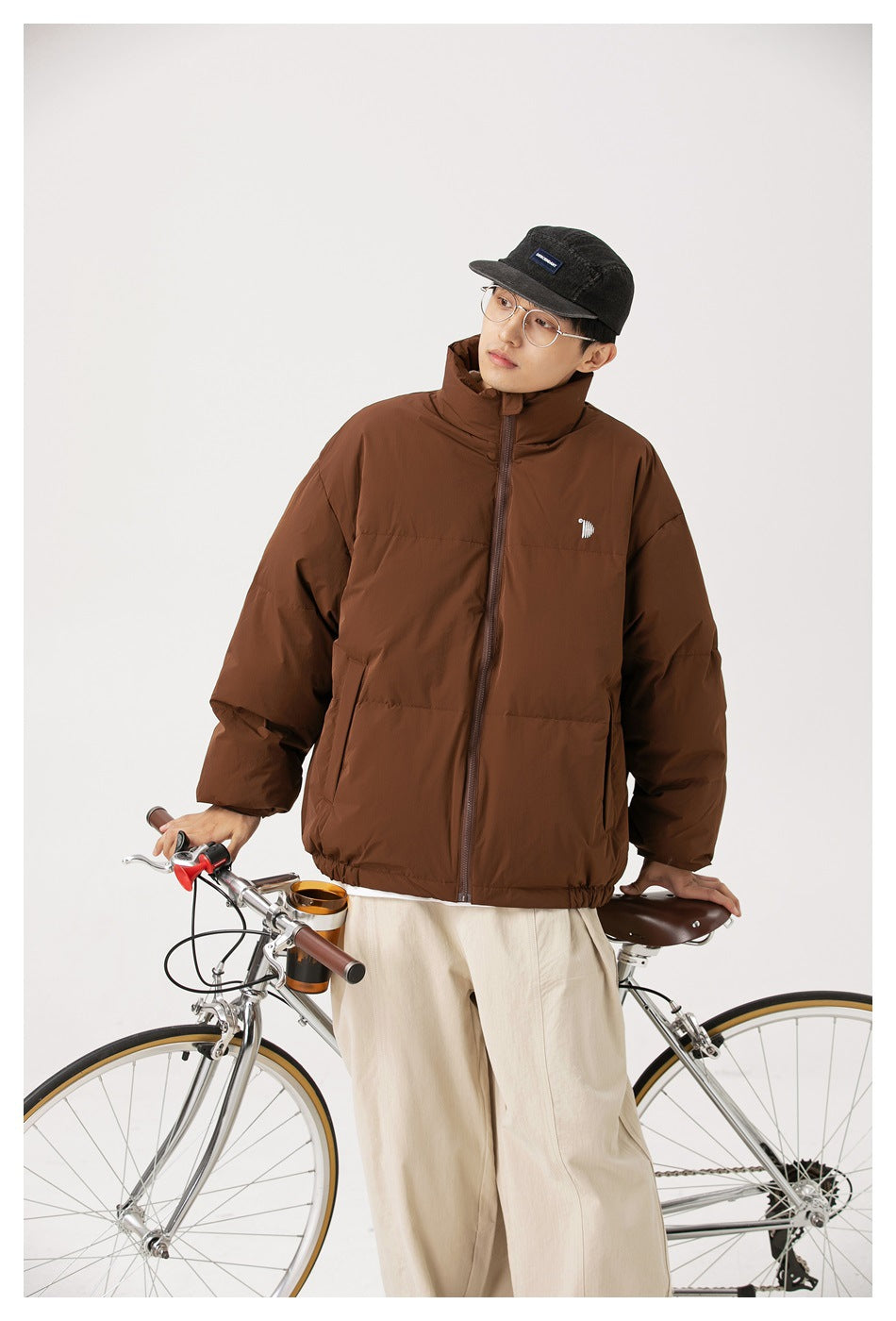 Front view of a model wearing a brown padded jacket with a high collar, front zipper, and small chest emblem.