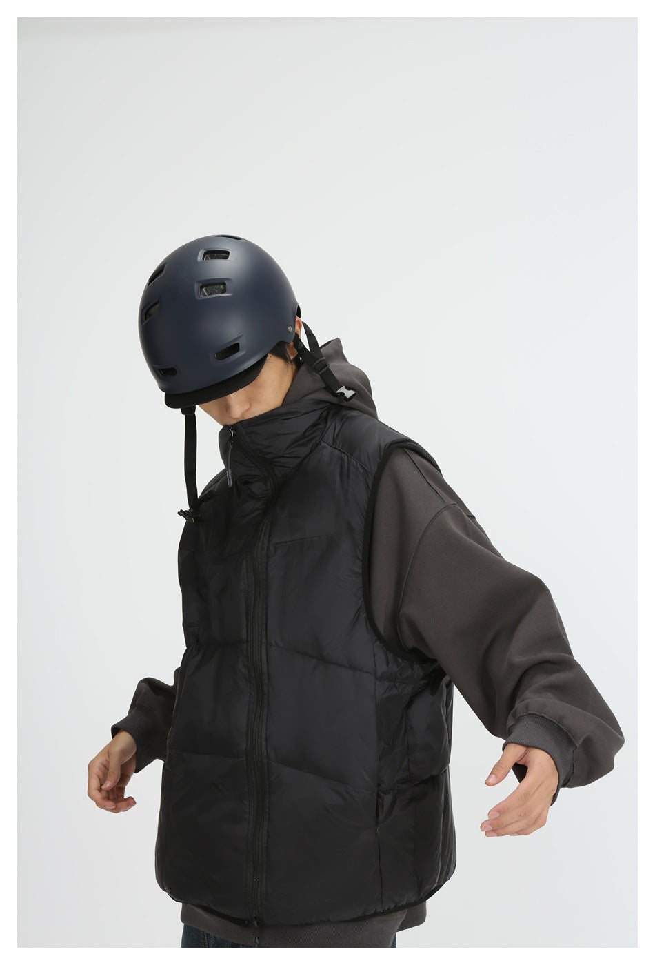Person in a helmet wearing a black quilted zip vest over a dark gray hoodie, head tilted down