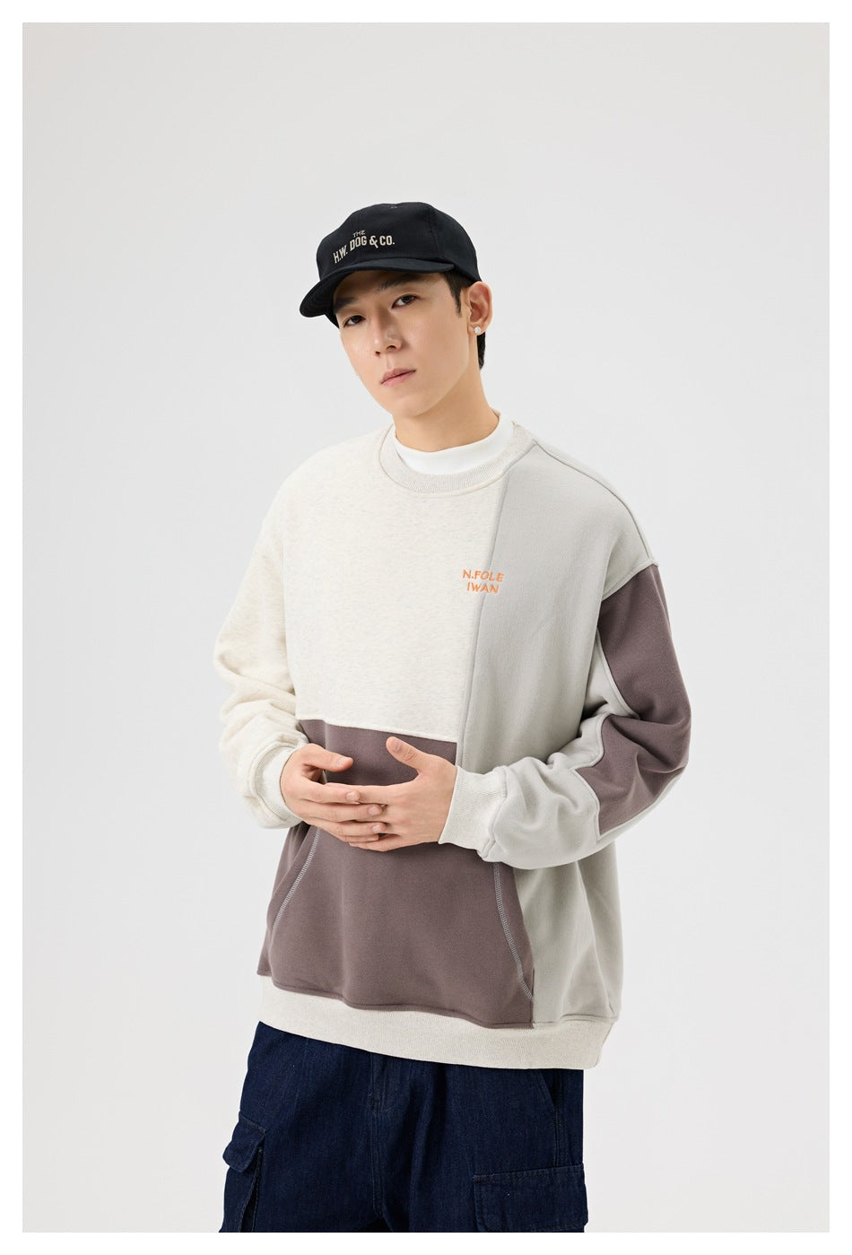 Model wearing a cream, light gray, and taupe color-block crewneck sweatshirt with a large front pocket.