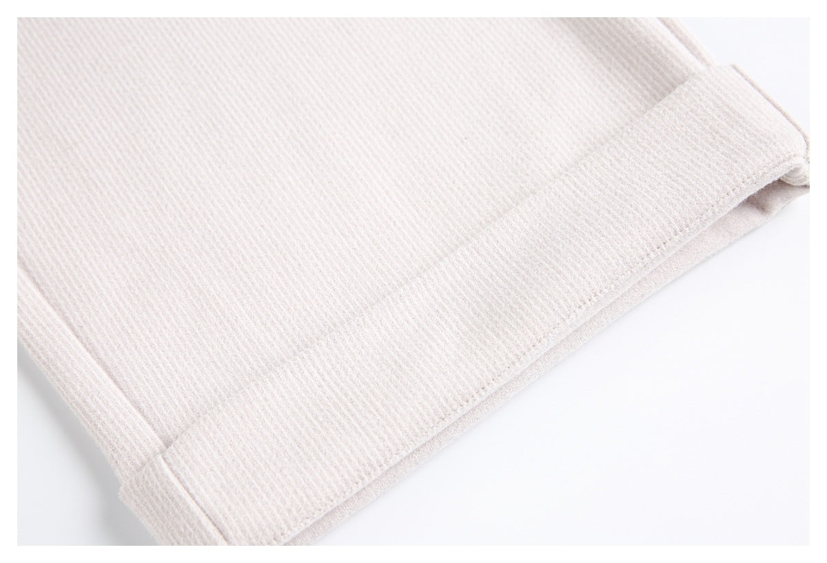 Close-up of the stitched hem on pale beige ribbed trousers.
