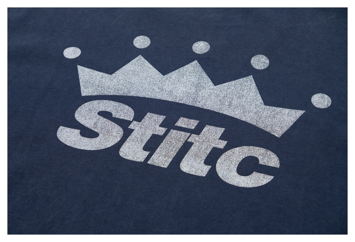 Close-up of a white crown and “Stilc” print on dark navy fabric.