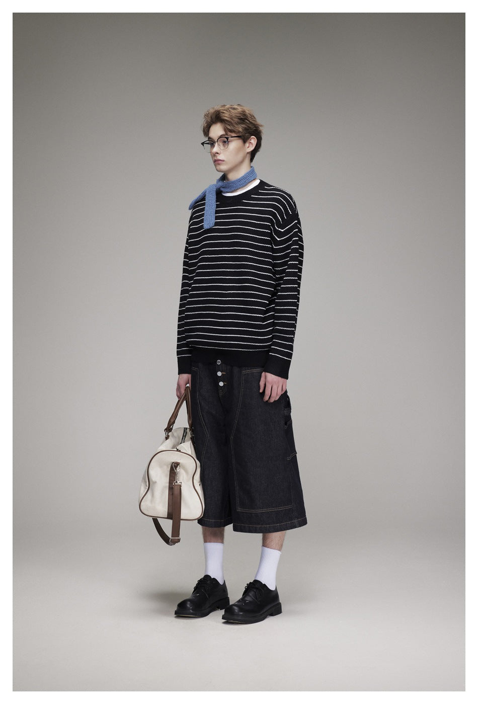 Three-quarter view of a model wearing a black sweater with white stripes, blue scarf, and dark denim shorts.