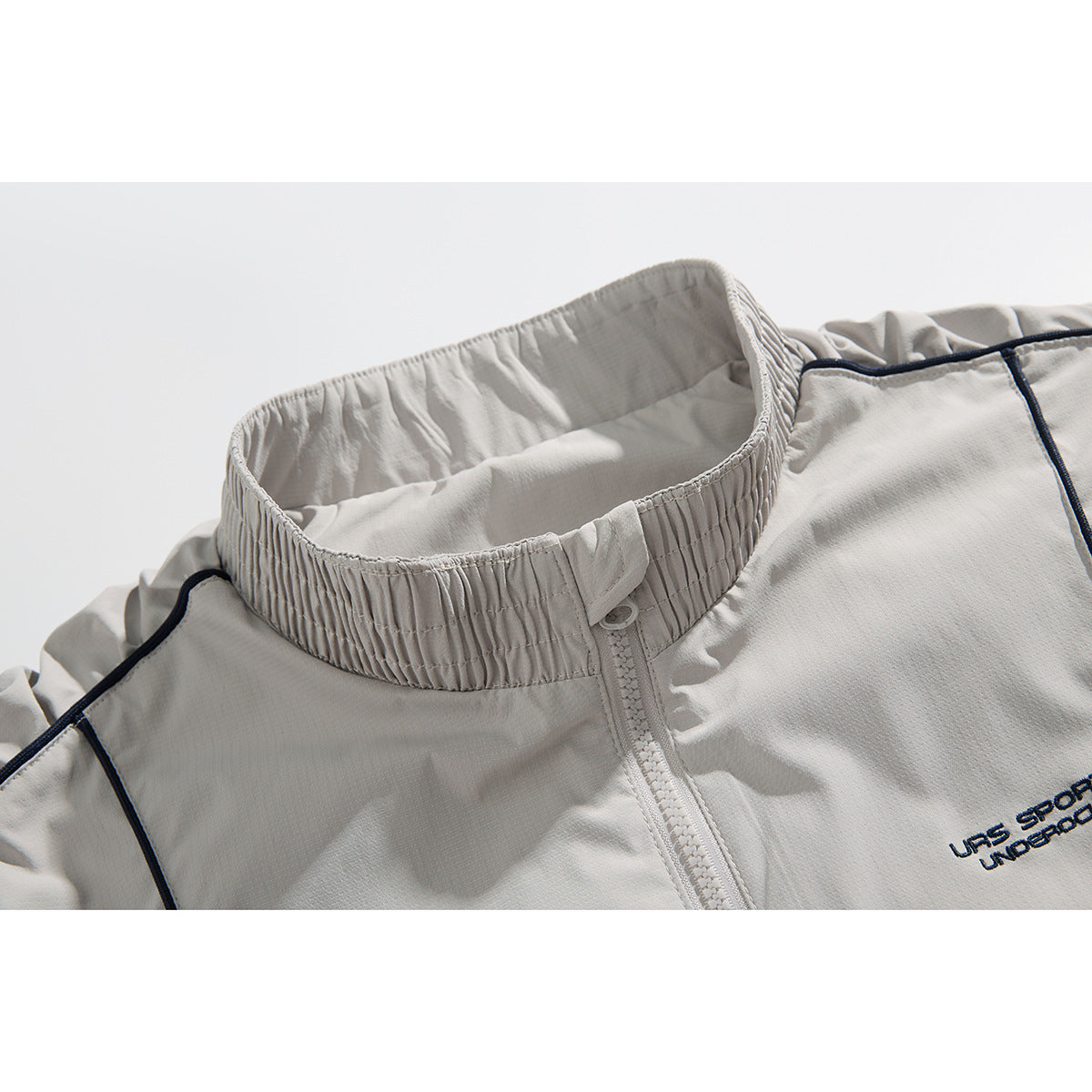 Close-up of a light gray zip-up jacket collar with a gathered stand collar and dark piping.