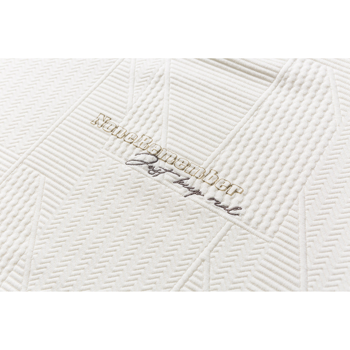 Close-up of small embroidered lettering on ivory fabric with raised geometric stitching.