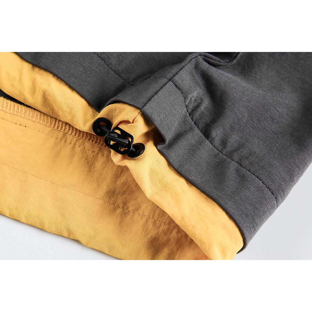 Close-up of charcoal fabric, mustard-yellow lining, and a black toggle fastening at a seam.