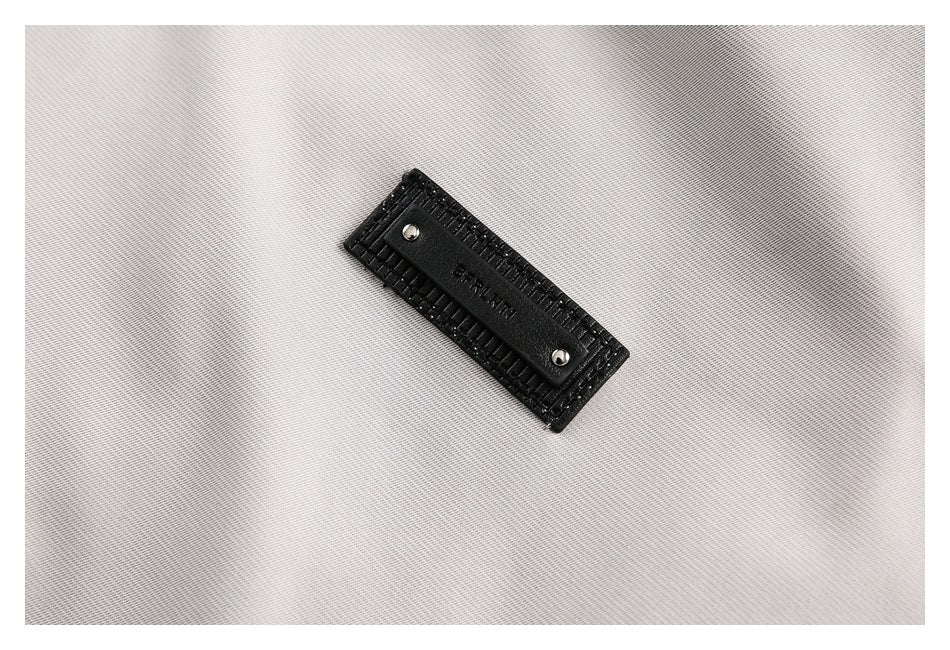 Close-up of a small black rectangular brand patch attached to light gray jacket fabric.