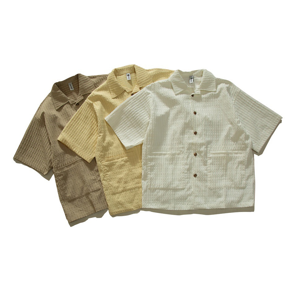 Three short-sleeve collared shirts arranged together in brown, pale yellow, and ivory.