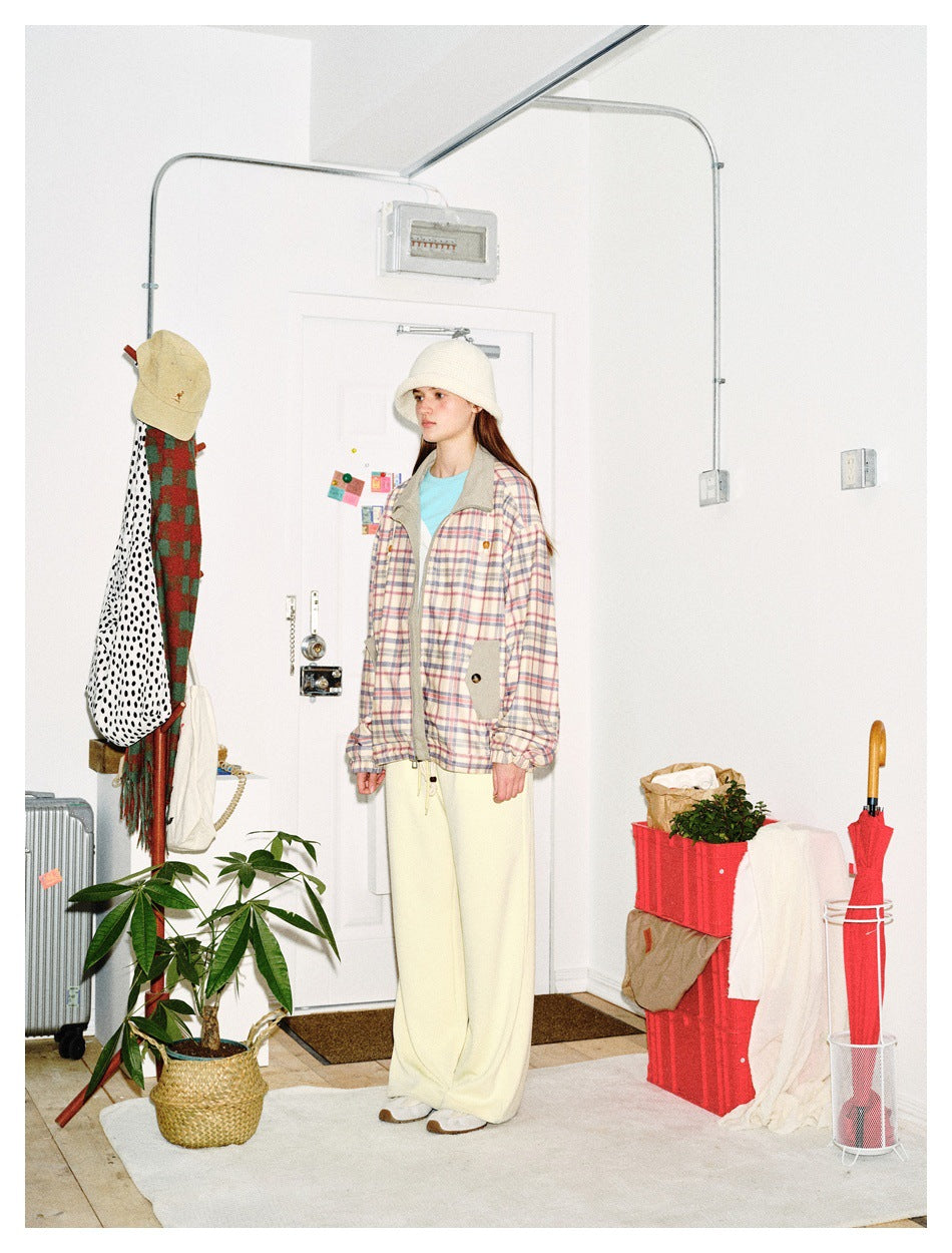 Three-quarter view of a model wearing a pastel plaid jacket with gray panels and cream wide-leg pants.