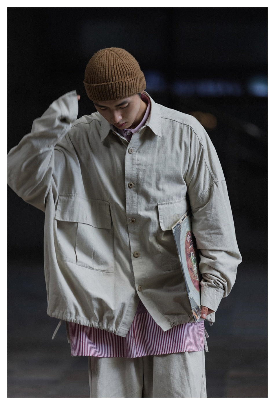 Front view of a model wearing a light gray oversized jacket with large flap pockets over a pink striped shirt.