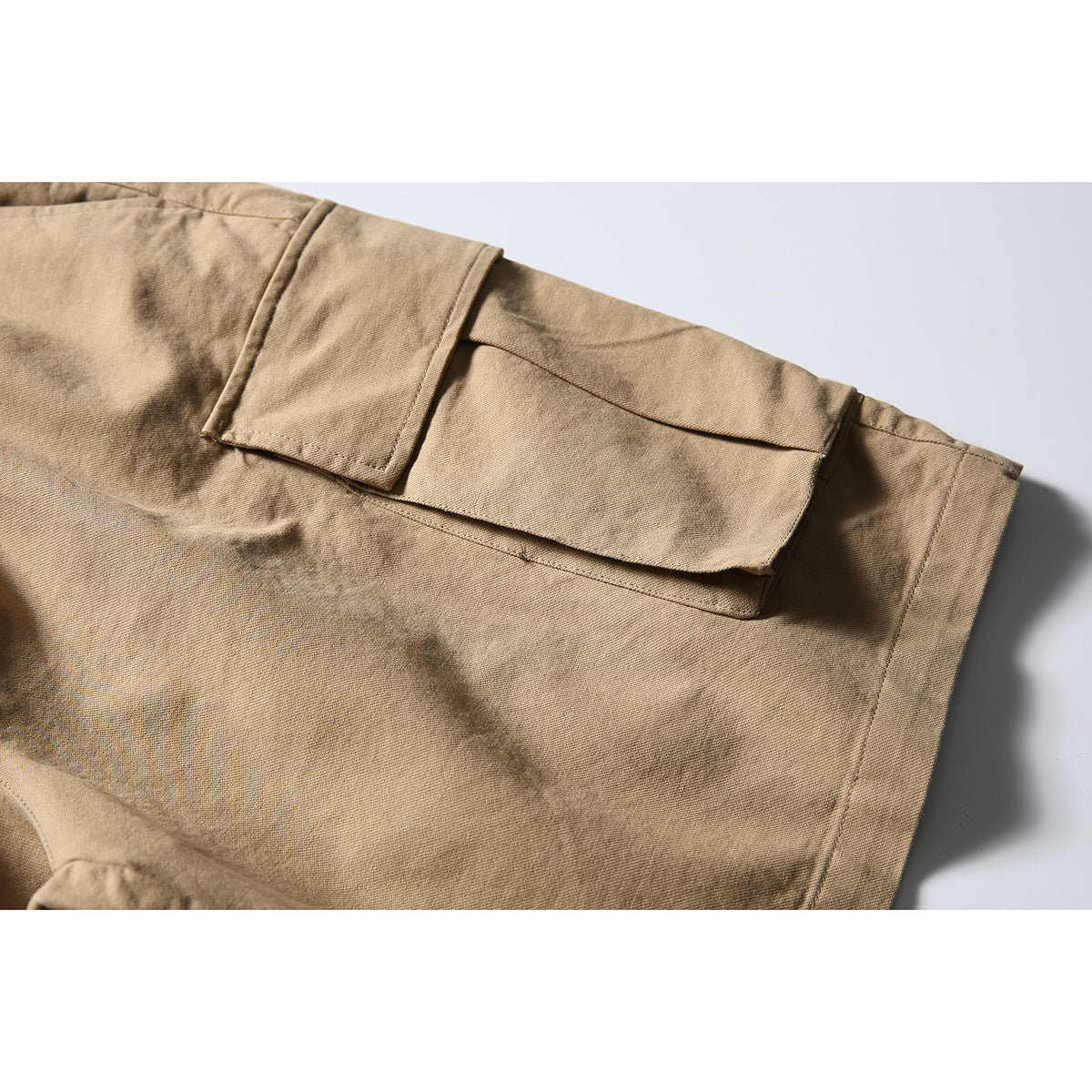 Close-up of tan cargo shorts showing a large flap pocket and surrounding seams.