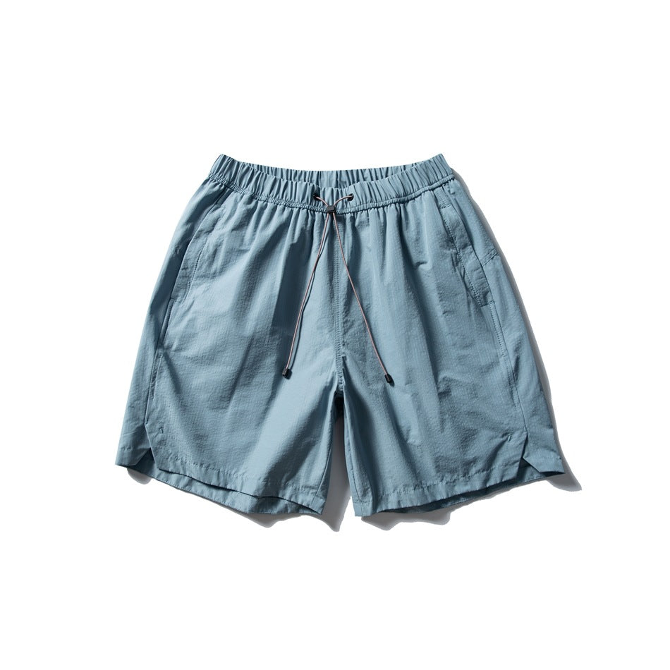 Dusty blue drawstring shorts with elastic waistband, side pockets and curved side-slit hems, flat lay