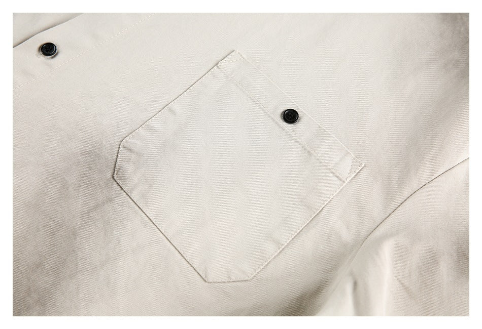 Close-up of a beige shirt's stitched chest pocket and black button.