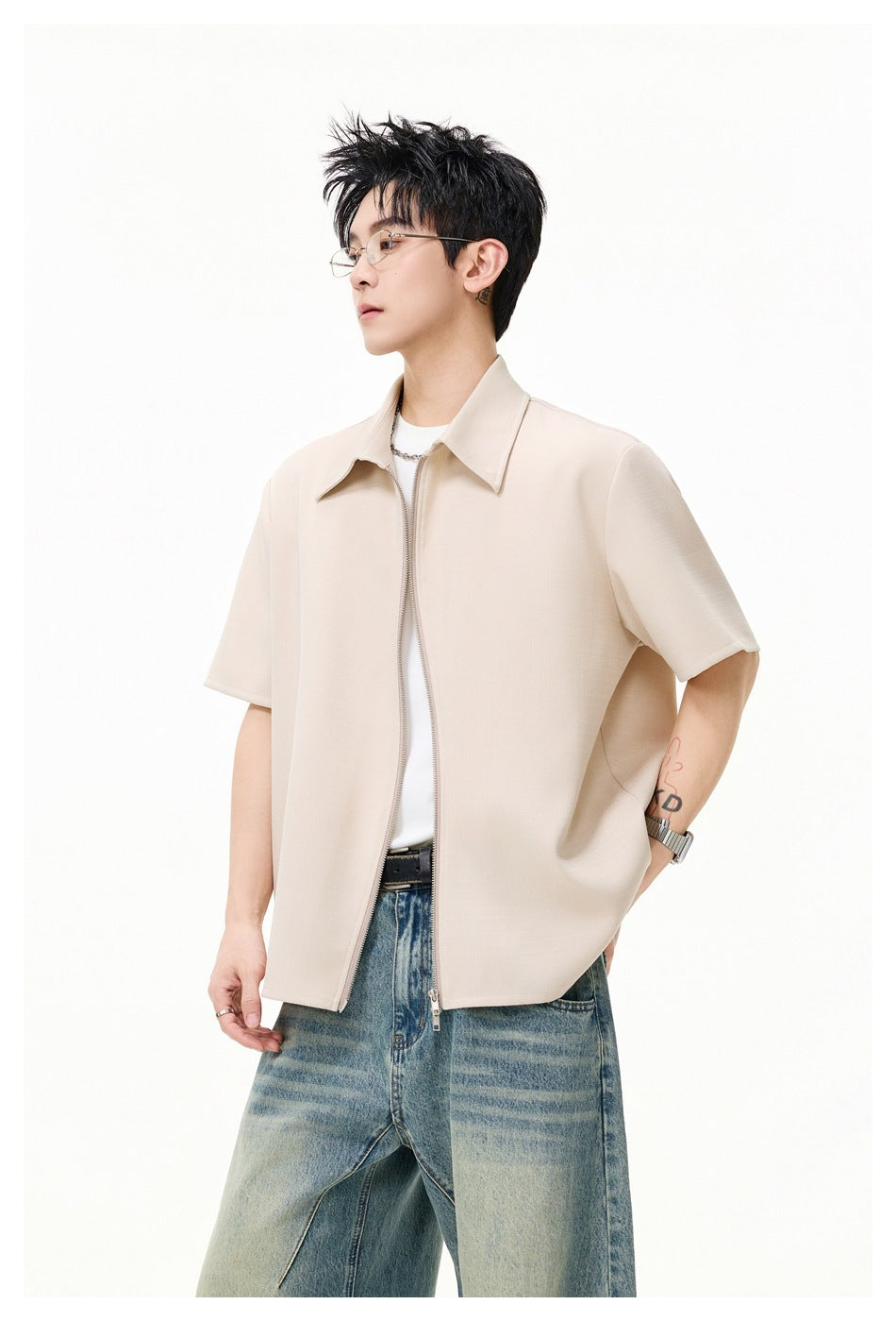 Model wearing a light beige short-sleeve collared shirt with a front zipper over a white tee and blue jeans.