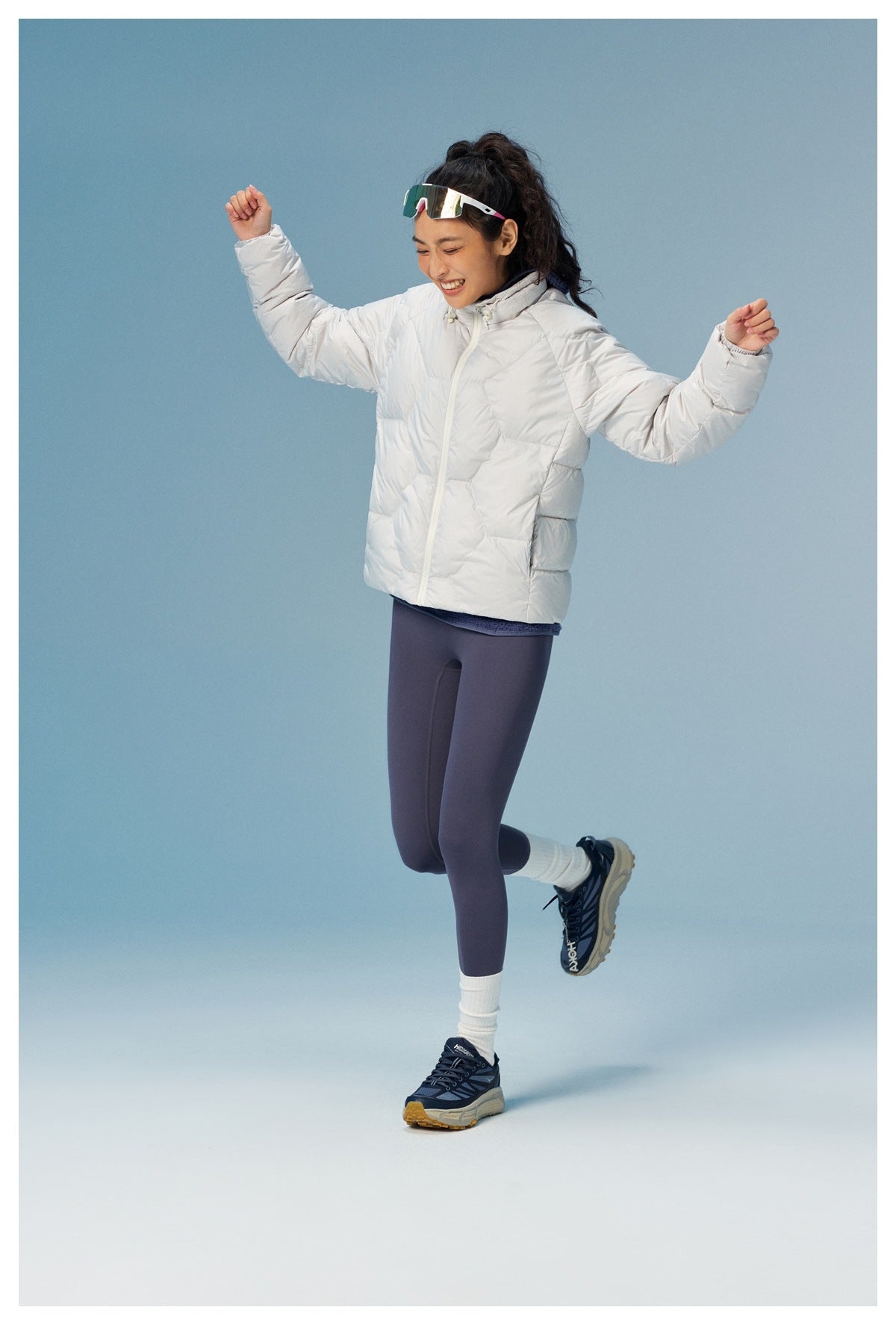 Woman in a white quilted puffer jacket and dark leggings, shown posing with arms raised.