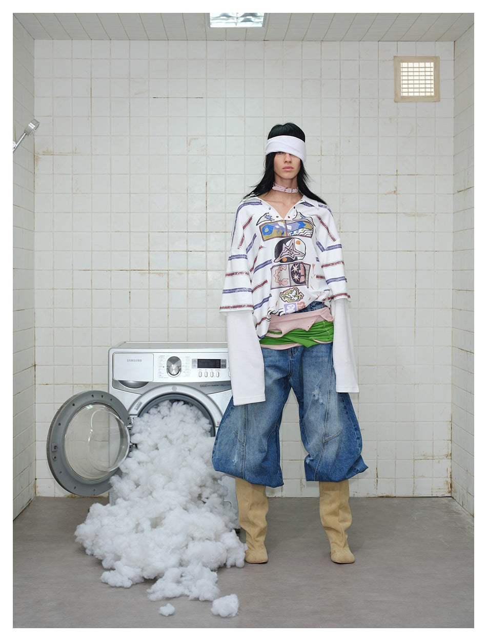 Model wearing a white graphic polo with long undersleeves and loose blue jeans in a tiled laundry room.