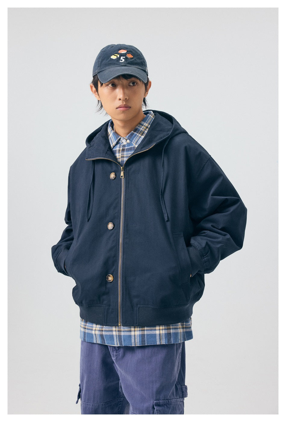 Front view of a model wearing a navy hooded jacket with a gold-tone zipper, buttons and front pockets.