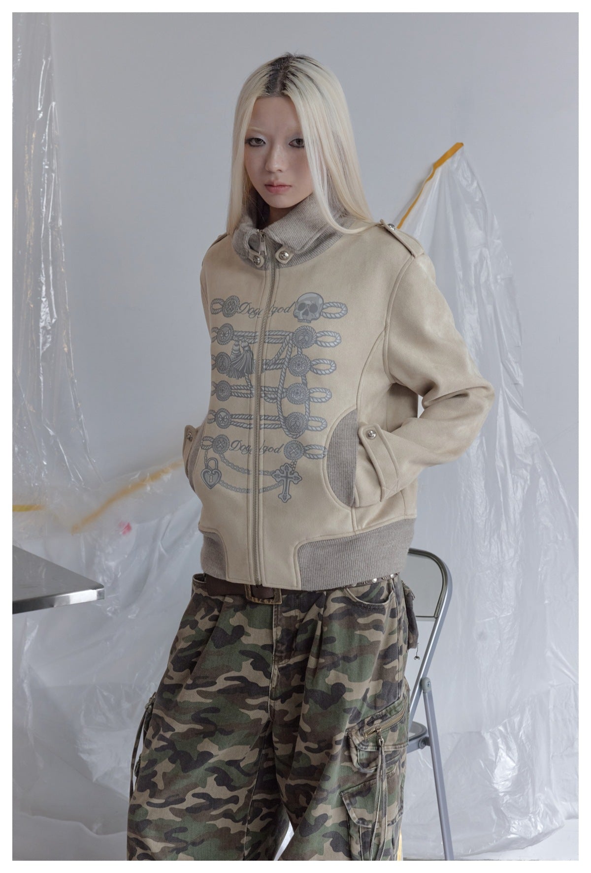 Model wearing a beige graphic zip jacket with gray ribbed trim and green camouflage cargo pants.