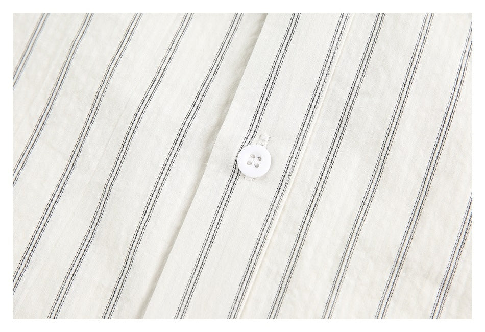 Close-up of a white button on the placket of an ivory shirt with thin dark stripes.