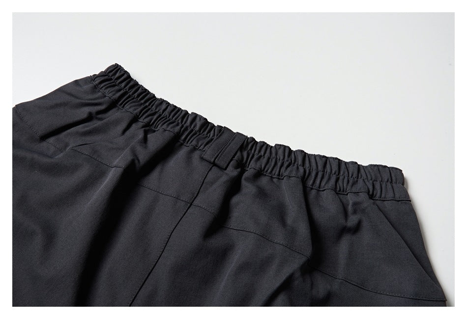 Close-up of the back of charcoal trousers with an elastic waistband, belt loop, and rear pockets.
