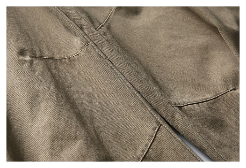 Close-up of taupe trousers showing stitched seams and overlapping pocket panels.