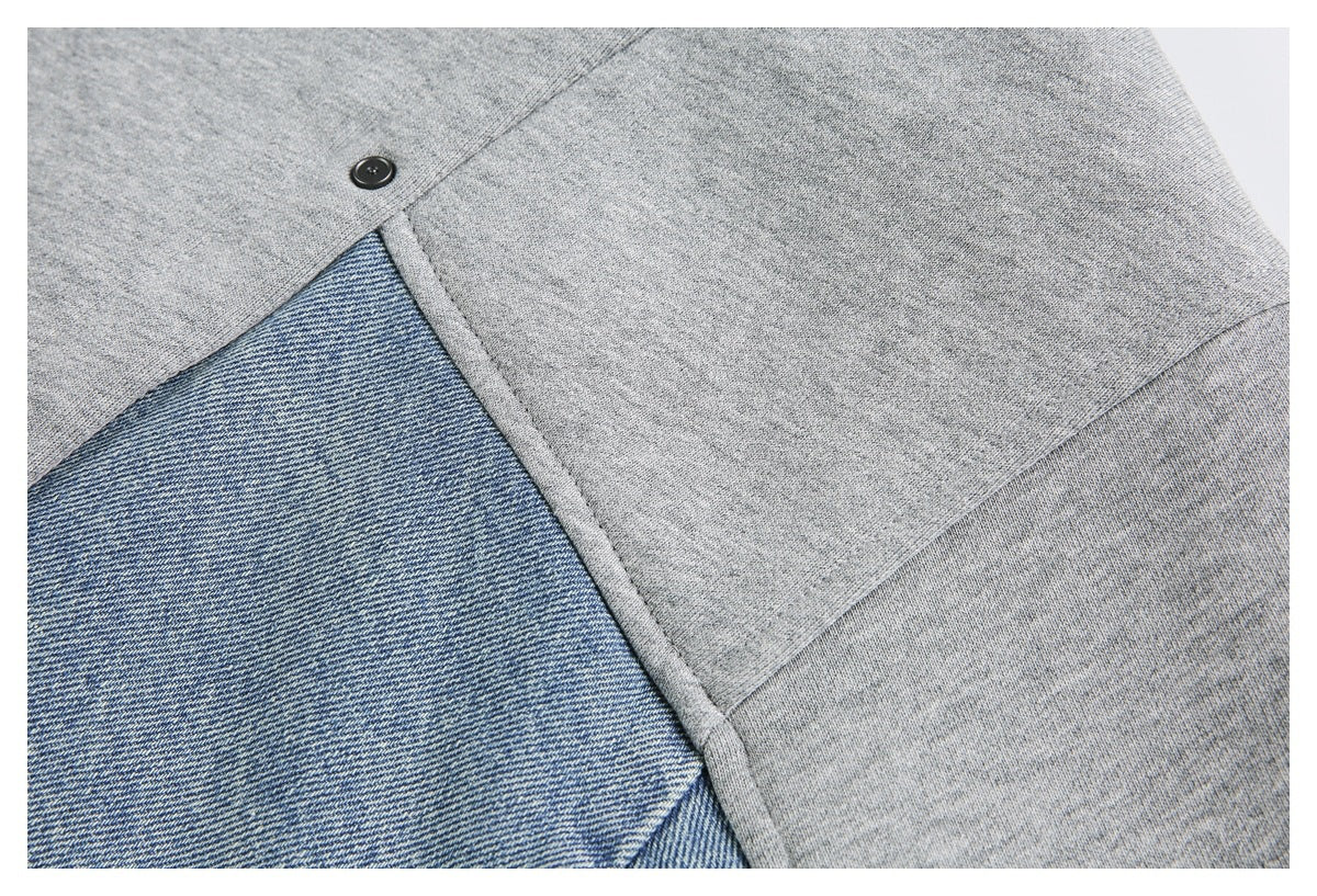 Close-up of a black snap fastener where a gray knit panel meets blue denim fabric.