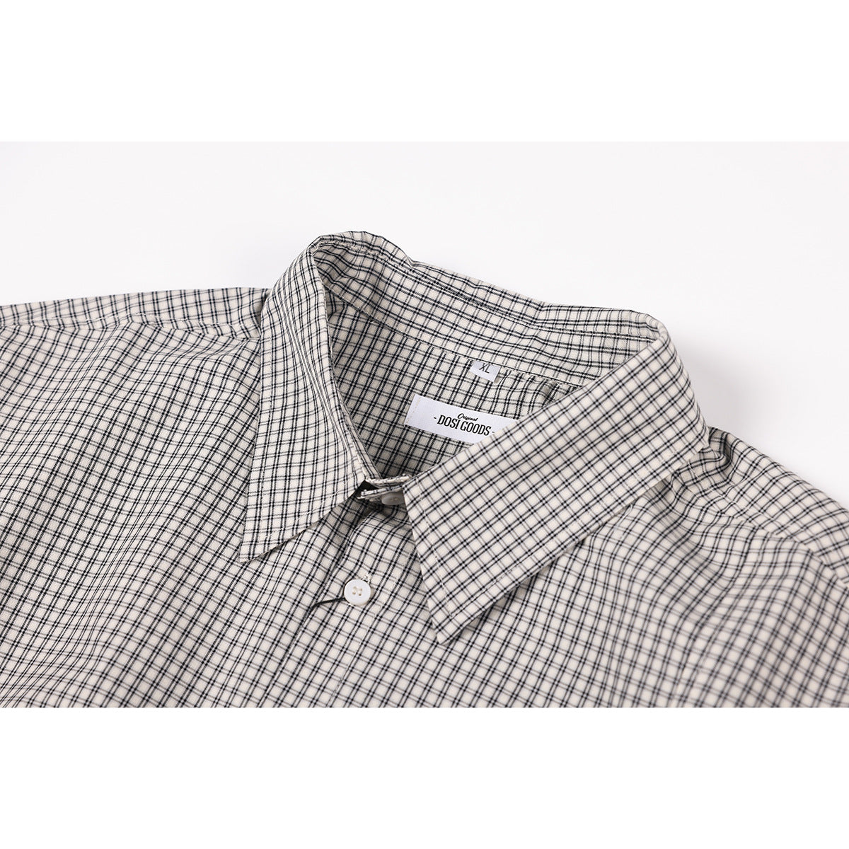 Close-up of a white shirt with a black windowpane check, pointed collar, button, and sewn-in neck label.