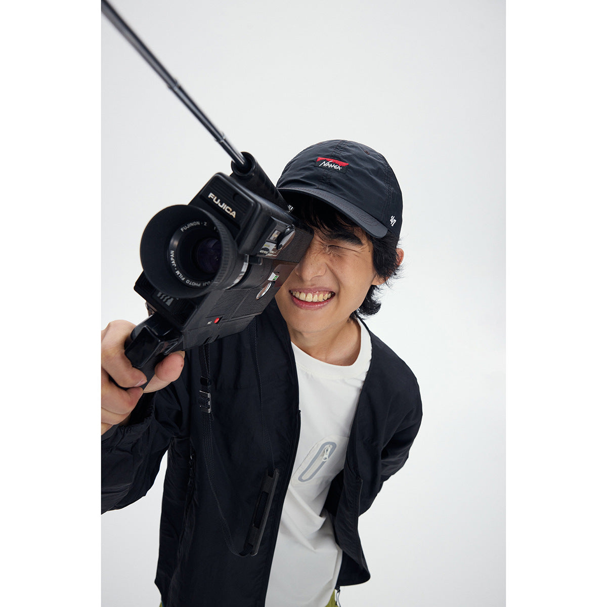 Close-up of a smiling model wearing a black jacket over a white shirt and a black cap.