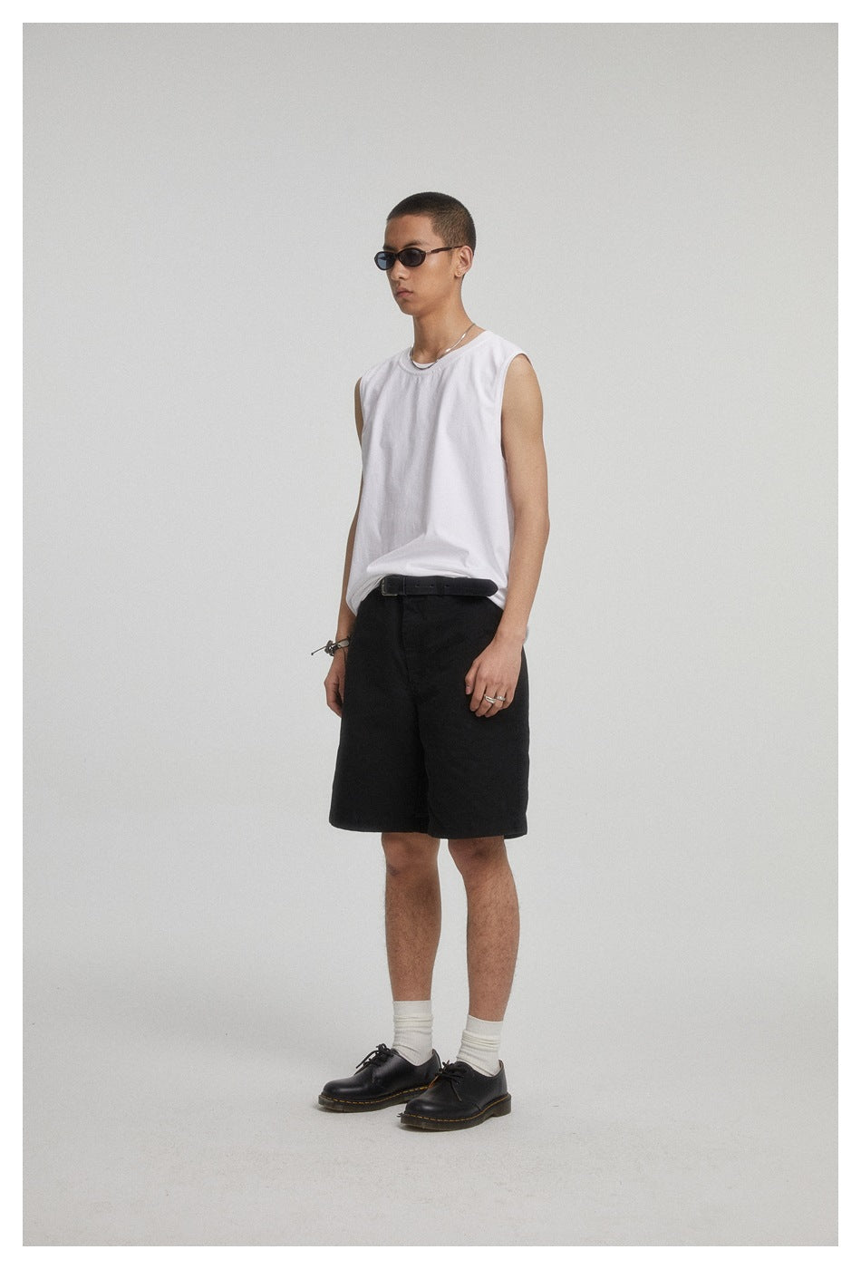 Model wearing a white sleeveless shirt and black shorts, shown against a plain studio backdrop.