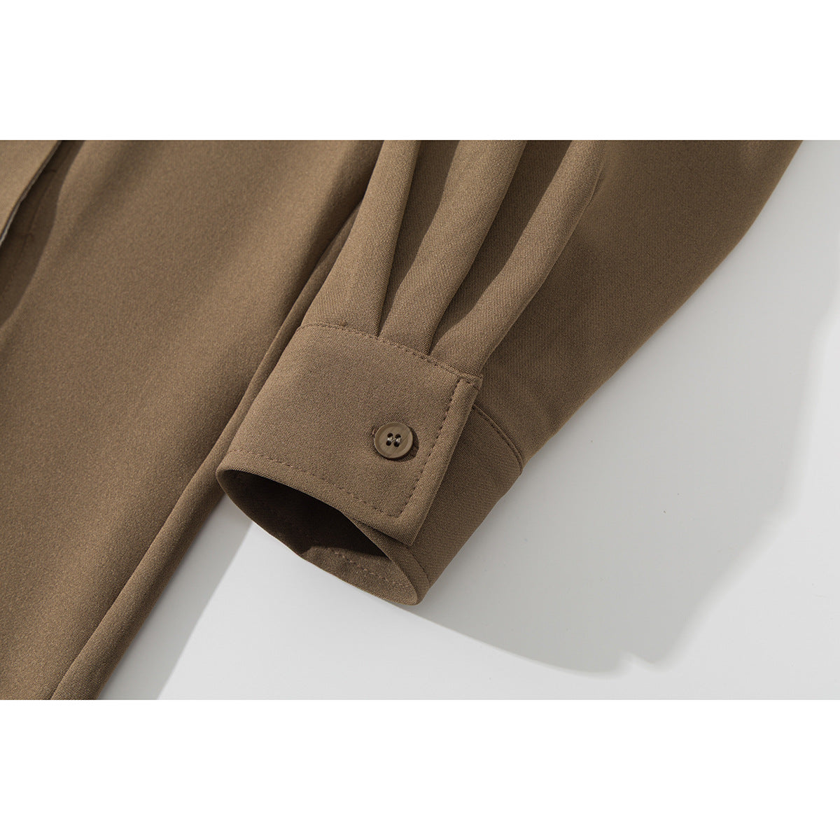 Close-up of a brown shirt sleeve cuff with a button and stitched pleats.
