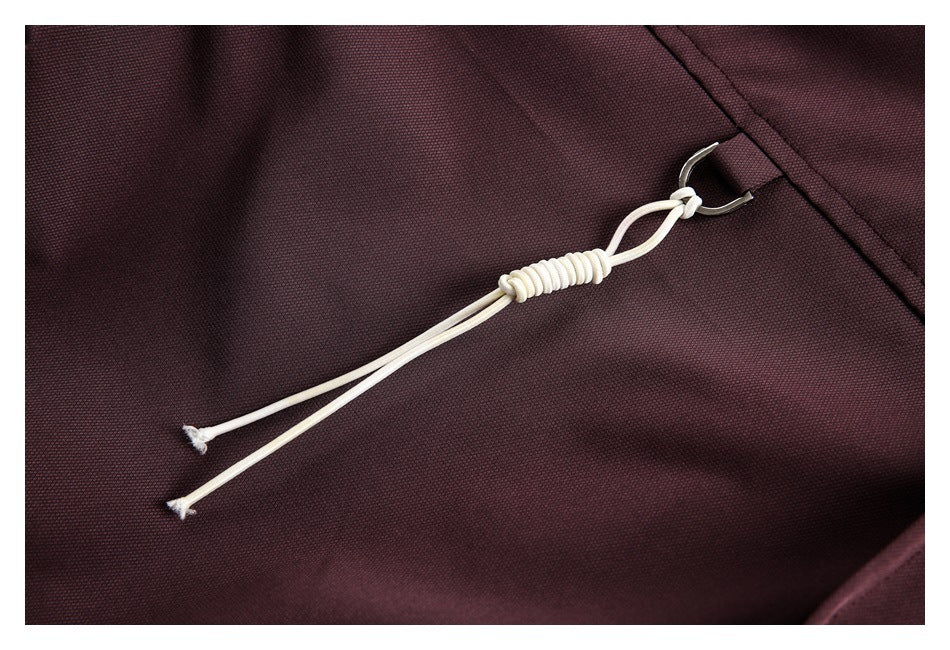 Close-up of a pale drawcord and metal hook on dark plum garment fabric.