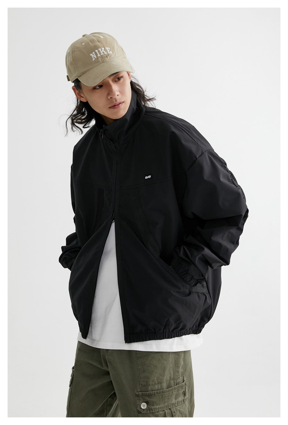 Model wearing a black zip-up jacket with a high collar, curved front pockets, and an elastic hem.