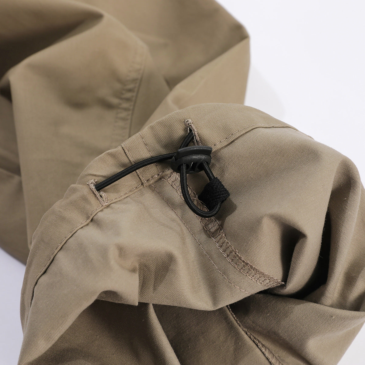Close-up of tan pants showing a black elastic drawcord and toggle at a seam.